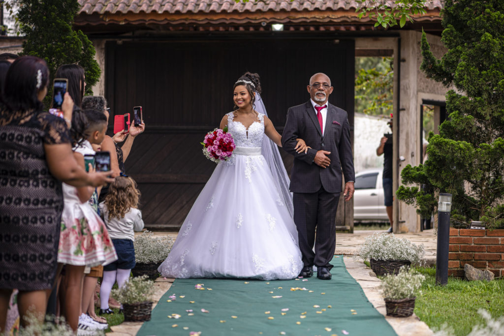 Noiva entrando no tapete verde do seu casamento ao ar livre.