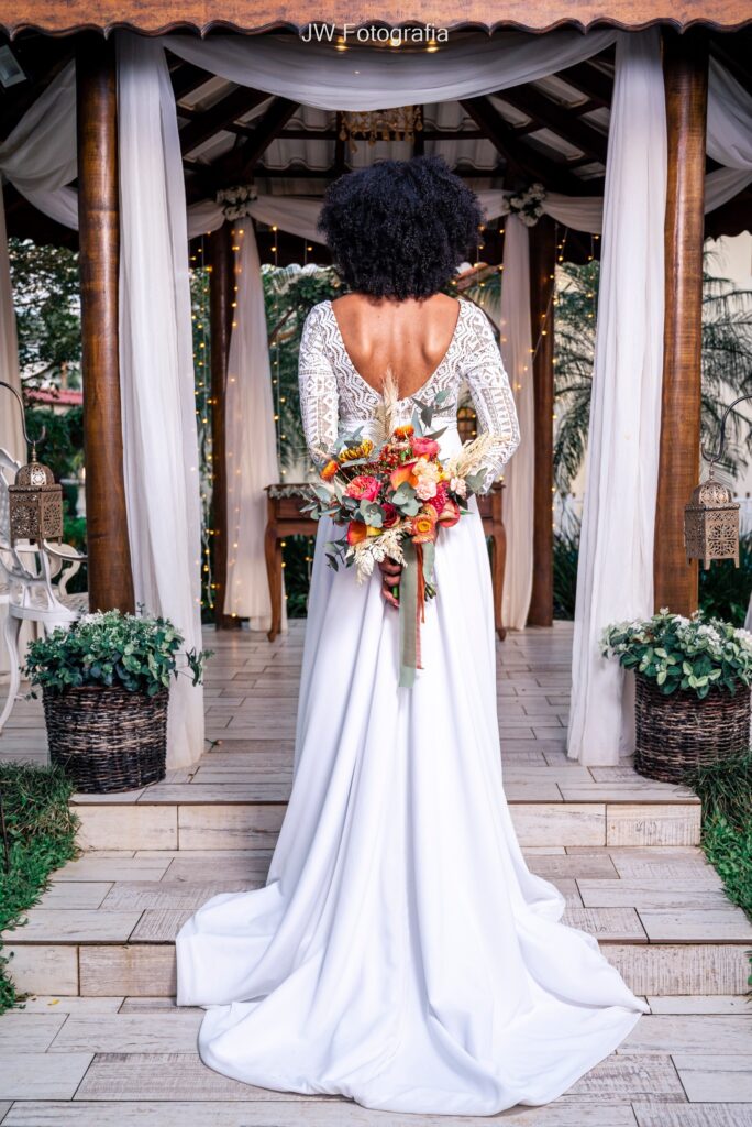 tendência buquê de noiva 2023 - noiva de costas exibindo os detalhes de seu vestido que combina com o buquê em tons quentes.